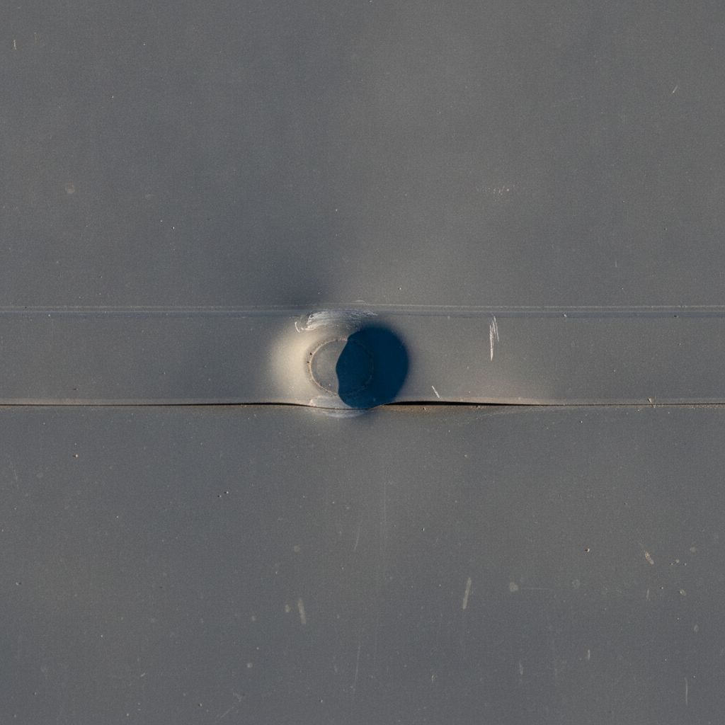 Hail impact dent on commercial metal roof panel surface near seam